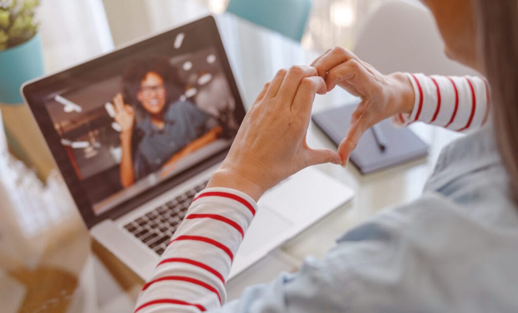 Woman doing hand heart gesture while talking with friend online