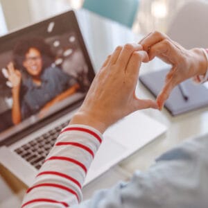 Woman doing hand heart gesture while talking with friend online