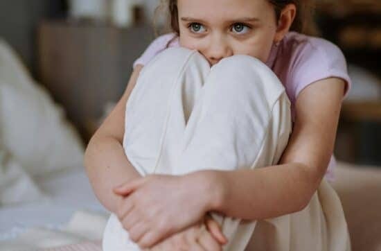 Little sad girl sitting alone on a bed.